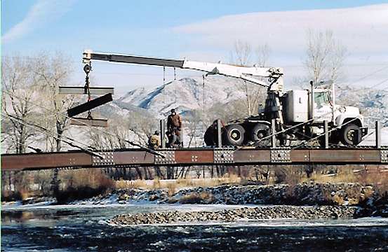 Like building a railroad, the boom truck backs over completed deck to set floor beams, three at a time.